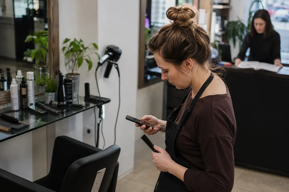 Właścicielka salonu kosmetycznego odpowiada klientce na telefonie, gdy w tle czeka kolejna rozmowa z komunikatora